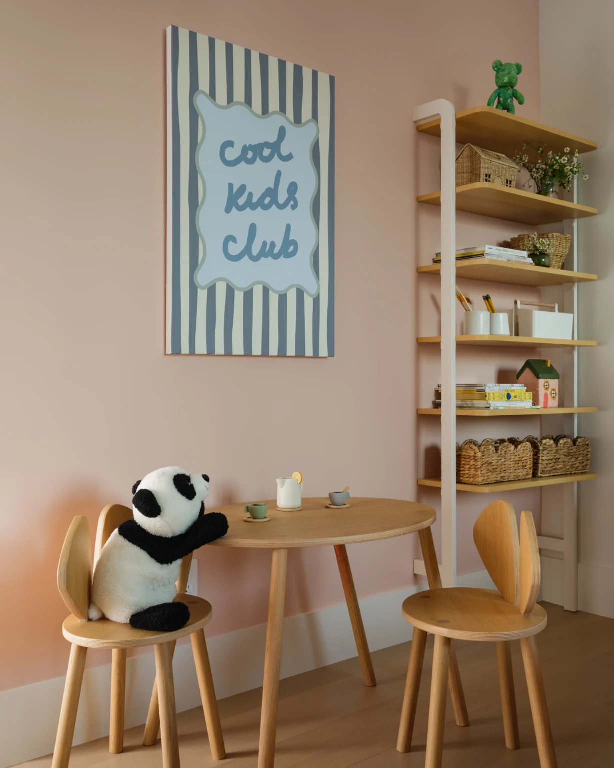Modern girls room play area interior design in a NYC apartment with pink walls, wood table, panda toy, custom shelves, and Cool Kids Club art