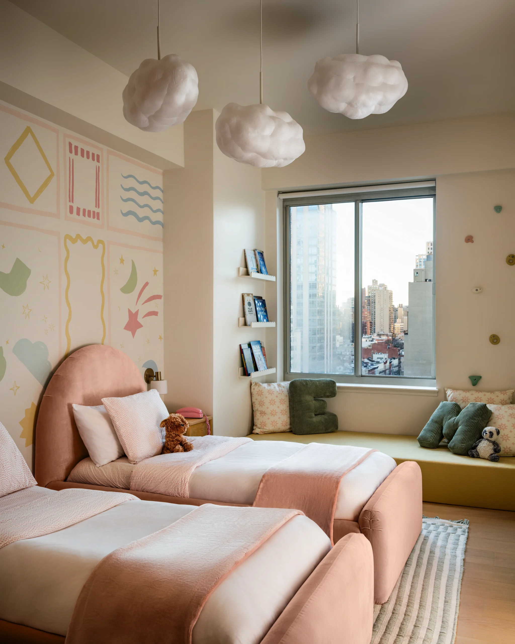 Fun pink girls bedroom interior design in a Manhattan apartment with twin beds, cloud pendant lights, custom wall design, and NYC window seat