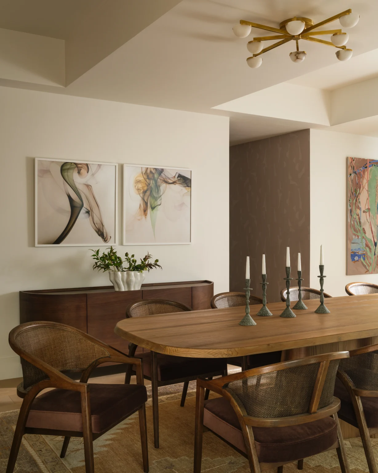 Modern tasteful dining room interior design in a NYC apartment with wood dining table, woven chairs, abstract art, and sculptural brass lighting