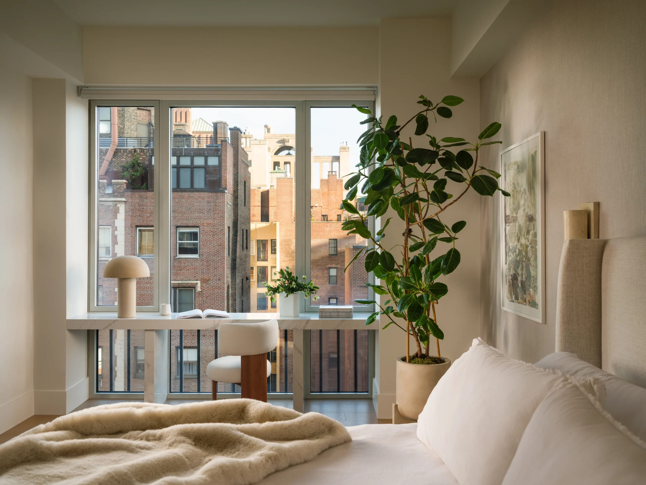 Wellness-focused primary bedroom in a Manhattan apartment with soft bedding, natural textures, indoor plant, and Upper East Side NYC views